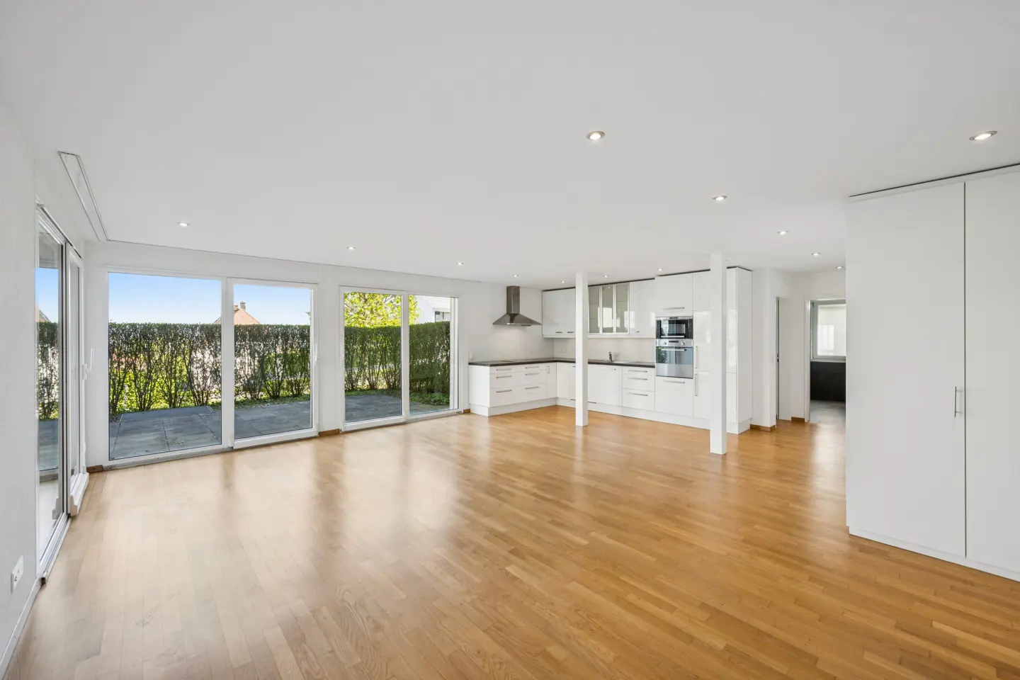 Bright, open-concept living space with hardwood floors, white kitchen cabinets, and sliding glass doors to a patio.