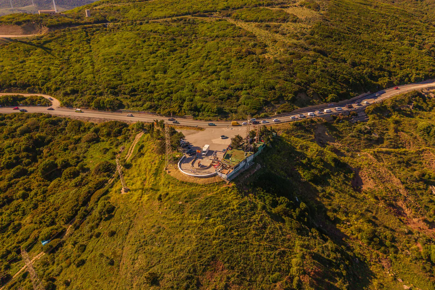 Aerial view of a green hillside with a road, cars, and a small parking area.