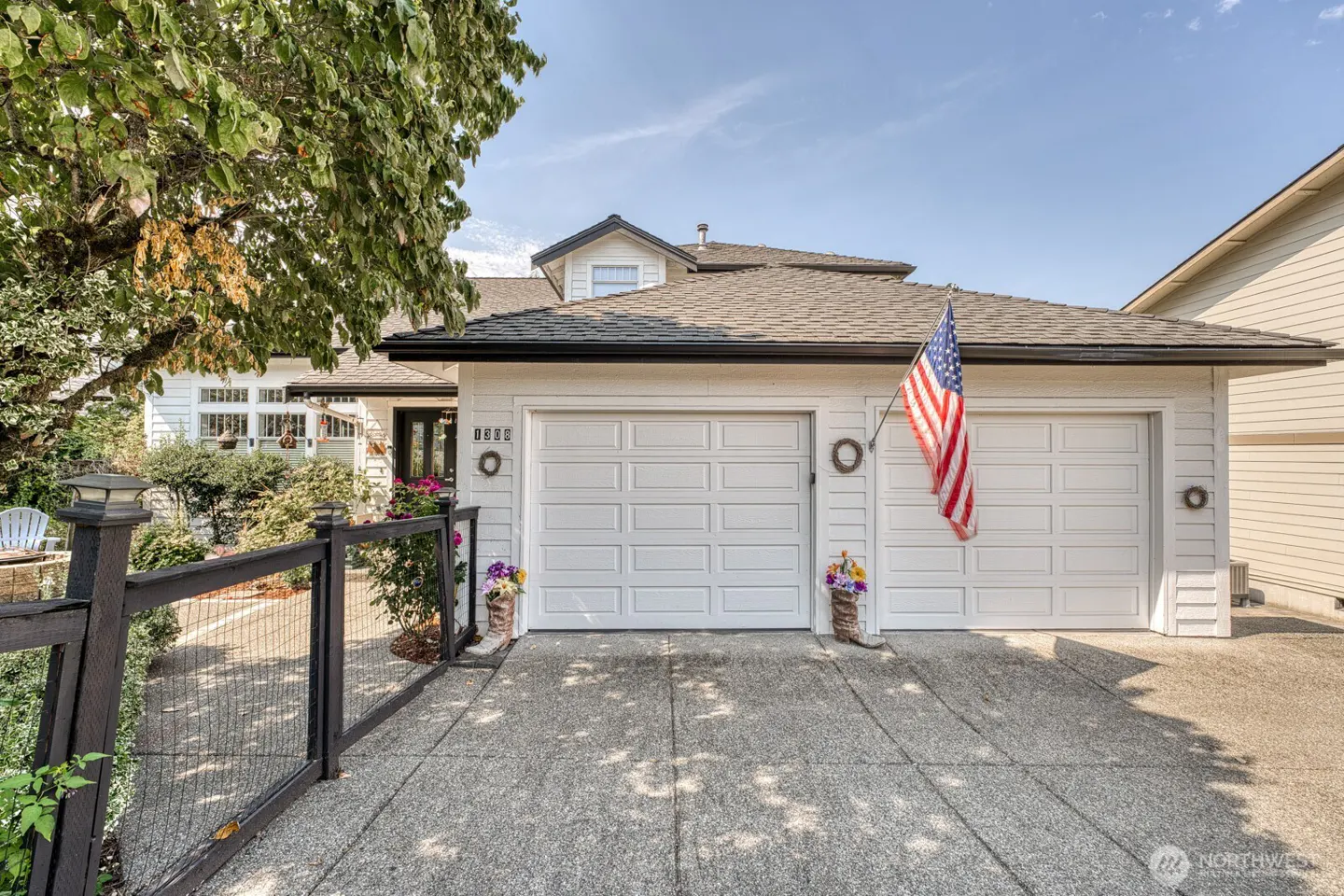 Exterior of a white house with a two-car garage, an American flag, and a black fence.