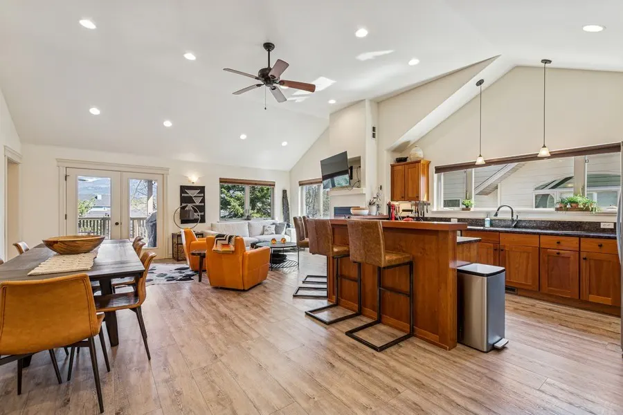 Open-concept living space with wood floors, dining table, orange chairs, kitchen island with stools, and a living room with a white sofa.