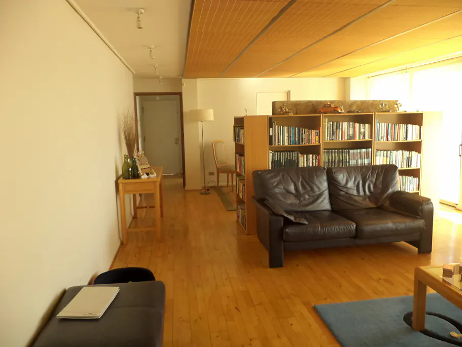 A living room with hardwood floors, a brown leather couch, and a bookshelf filled with books.