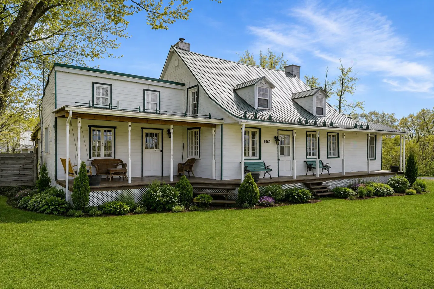 Exterior of a two-story white house with a metal roof, green trim, and a covered porch with seating.
