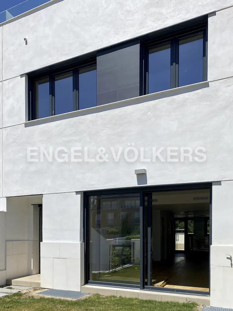Exterior view of a modern, two-story white house with black-framed windows and sliding glass doors. The Engel & Völkers logo is visible on the facade.