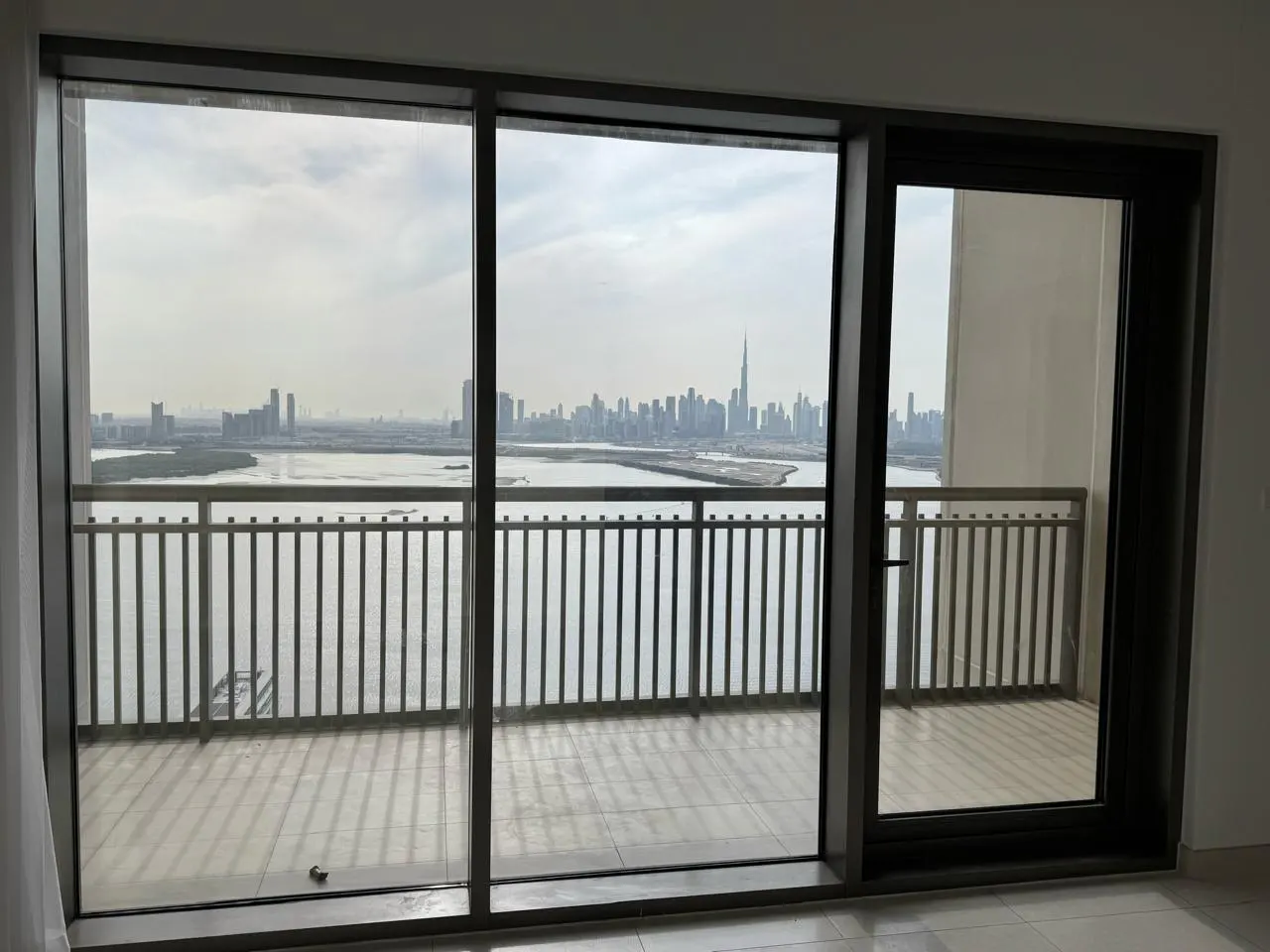 View from a high-rise balcony with gray railings overlooking the Dubai skyline and a body of water on a cloudy day.