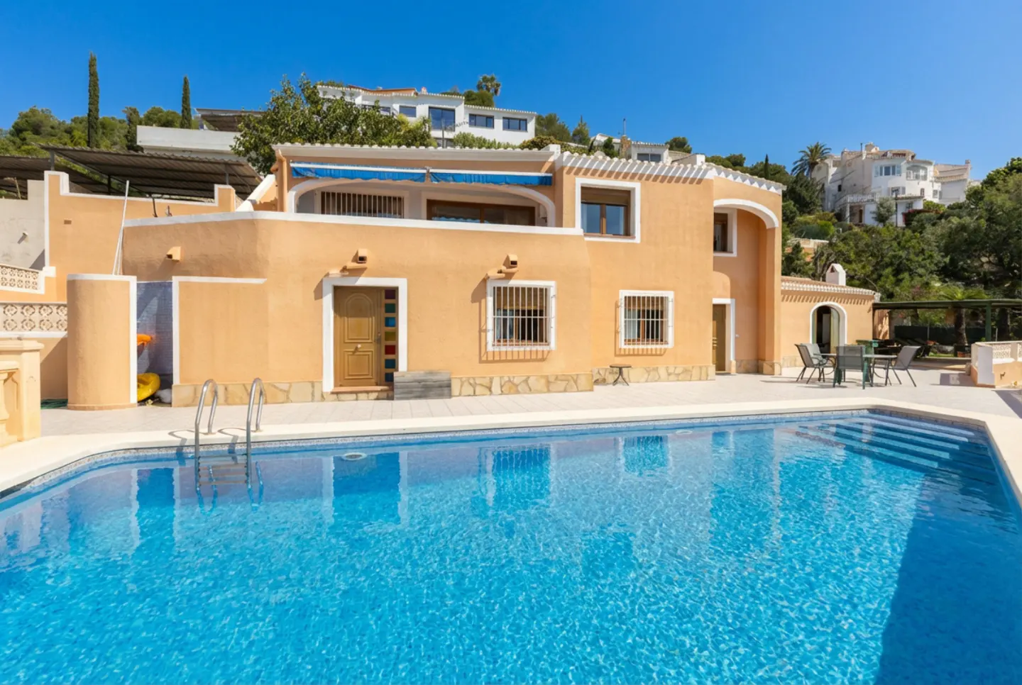 Exterior of a peach-colored house with a blue swimming pool in the foreground on a sunny day.
