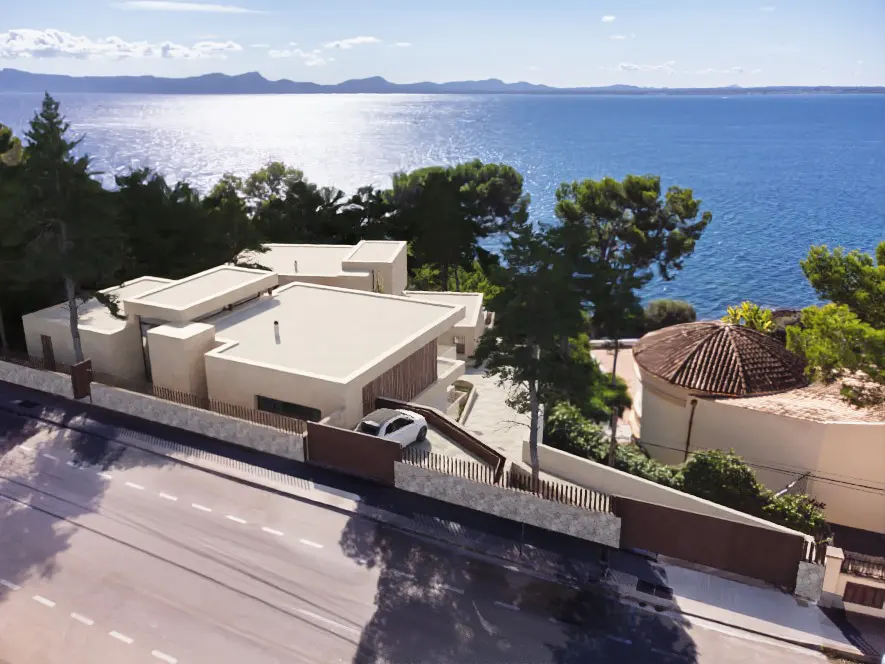 Aerial view of a modern, beige house with a flat roof, a car in the driveway, and the ocean in the background.