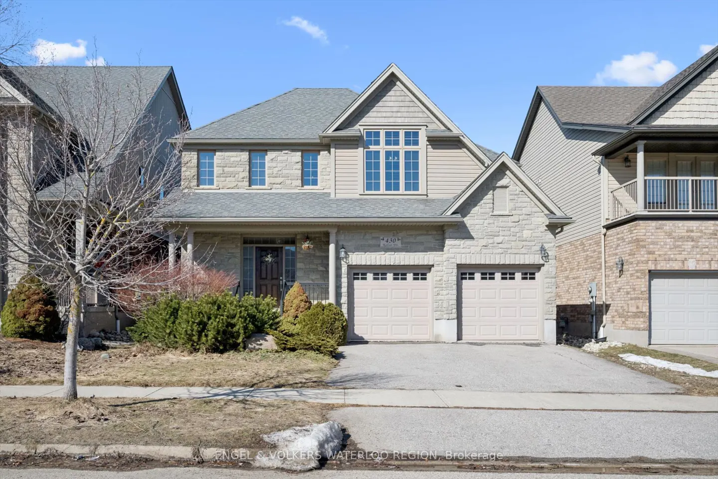 Two-story house with stone and beige siding, a gray roof, and a two-car garage on a sunny day.