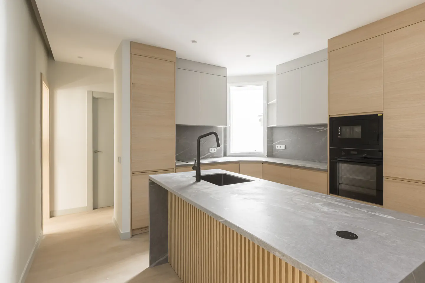 Bright kitchen with light wood cabinets, gray countertops, and a central island with a black faucet and sink.