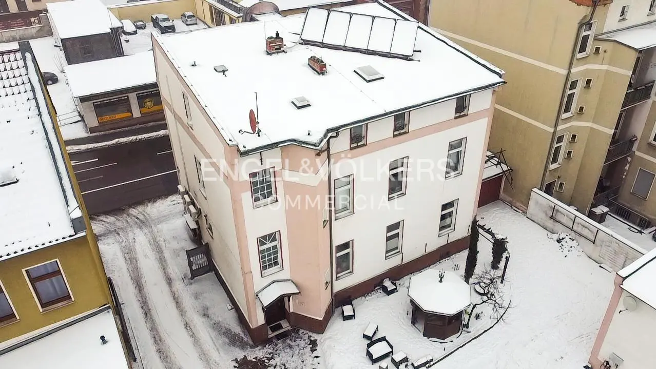 Aerial view of a snow-covered, three-story commercial building with white and pink facade, and an Engel & Völkers logo.