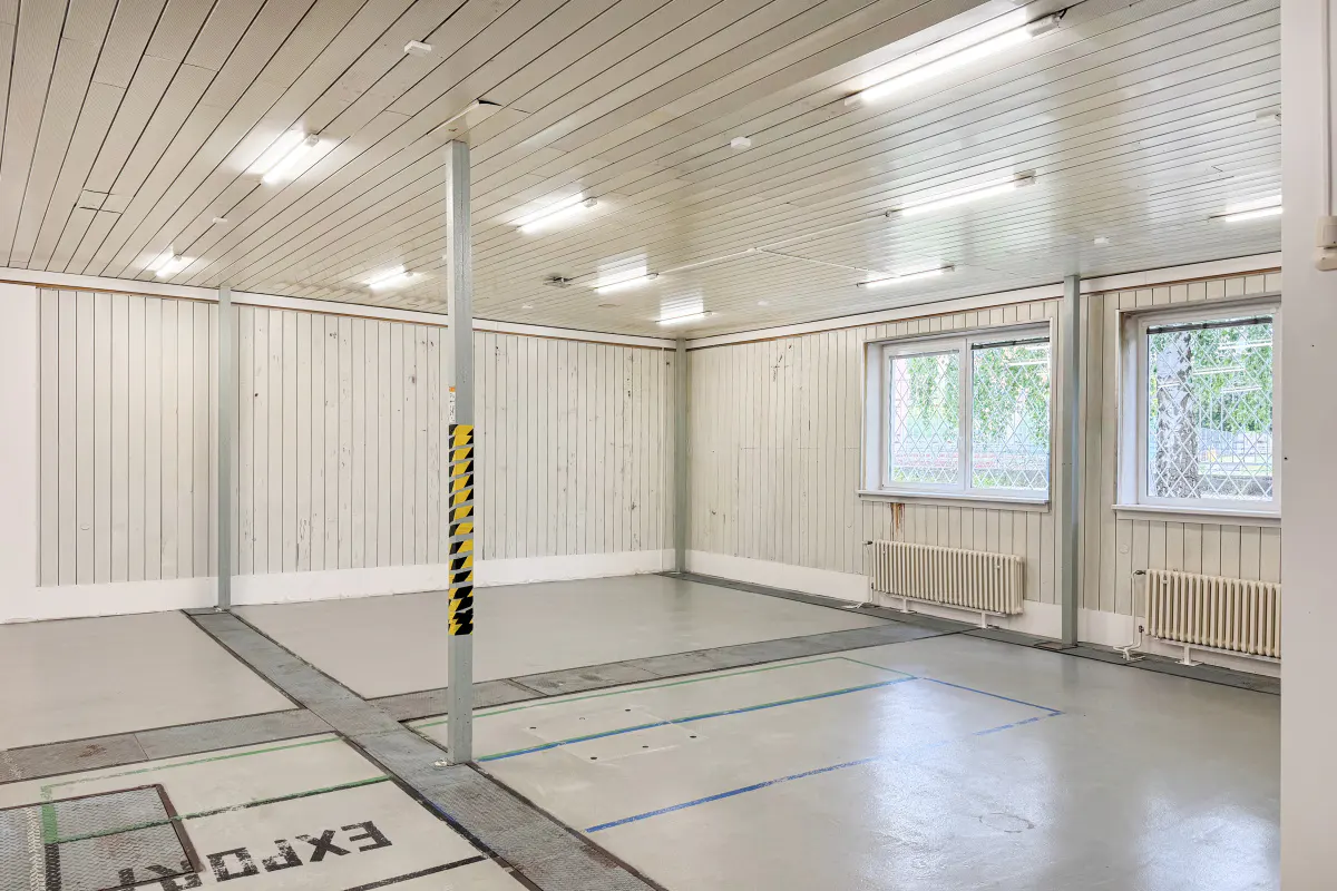 A large, empty room with white wood-paneled walls and ceiling, gray floor, and two windows.