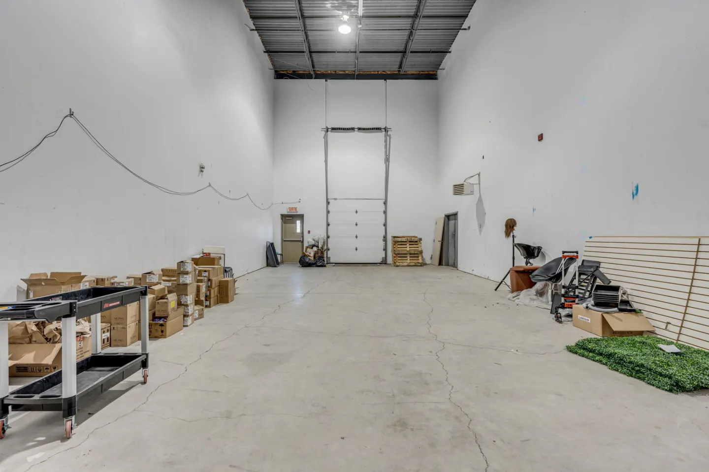 A large, empty commercial space with white walls, a concrete floor, and a metal ceiling. Boxes and equipment are scattered around the room.