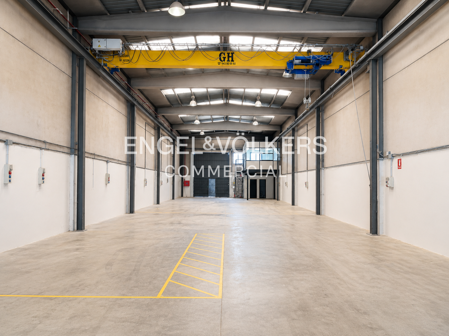 Spacious industrial warehouse with white walls, concrete floor, yellow overhead crane, and a small office area at the back.