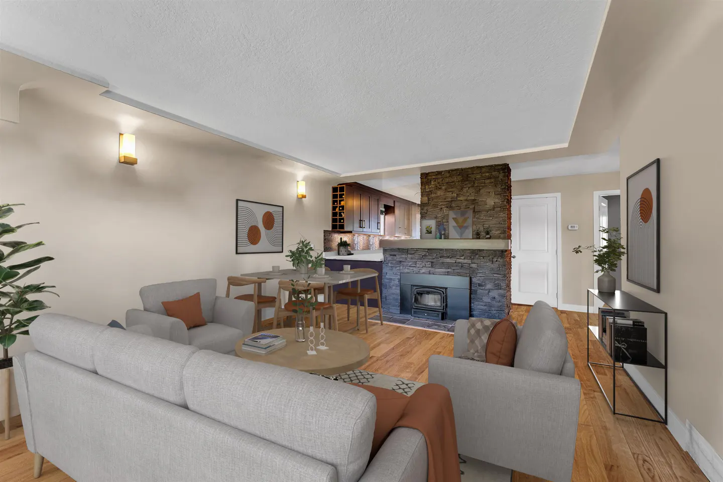 Living room with gray sofas, stone fireplace, and wood floors. Dining table and kitchen visible in the background.