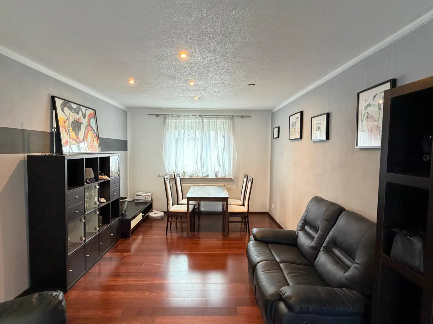 Living room with dark wood floors, gray walls, black sofa and shelving, and a dining table with four chairs. Artwork hangs on the walls.
