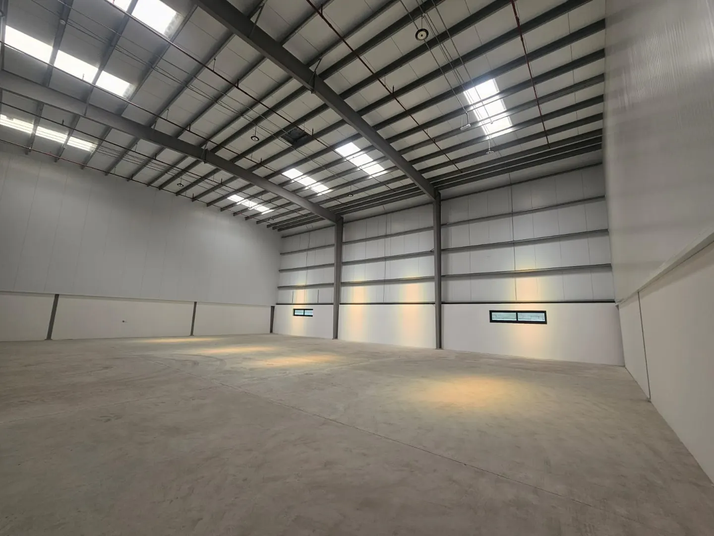 A large, empty warehouse with a concrete floor, white walls, and a high ceiling with skylights.