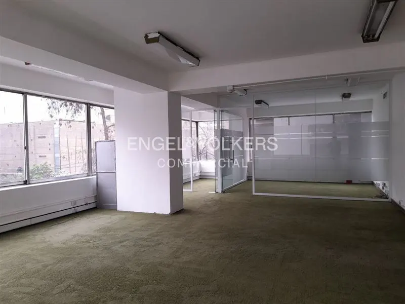 Empty office space with green carpet, white walls, and glass partitions. Engel & Volkers logo on a glass wall. Windows overlook trees.