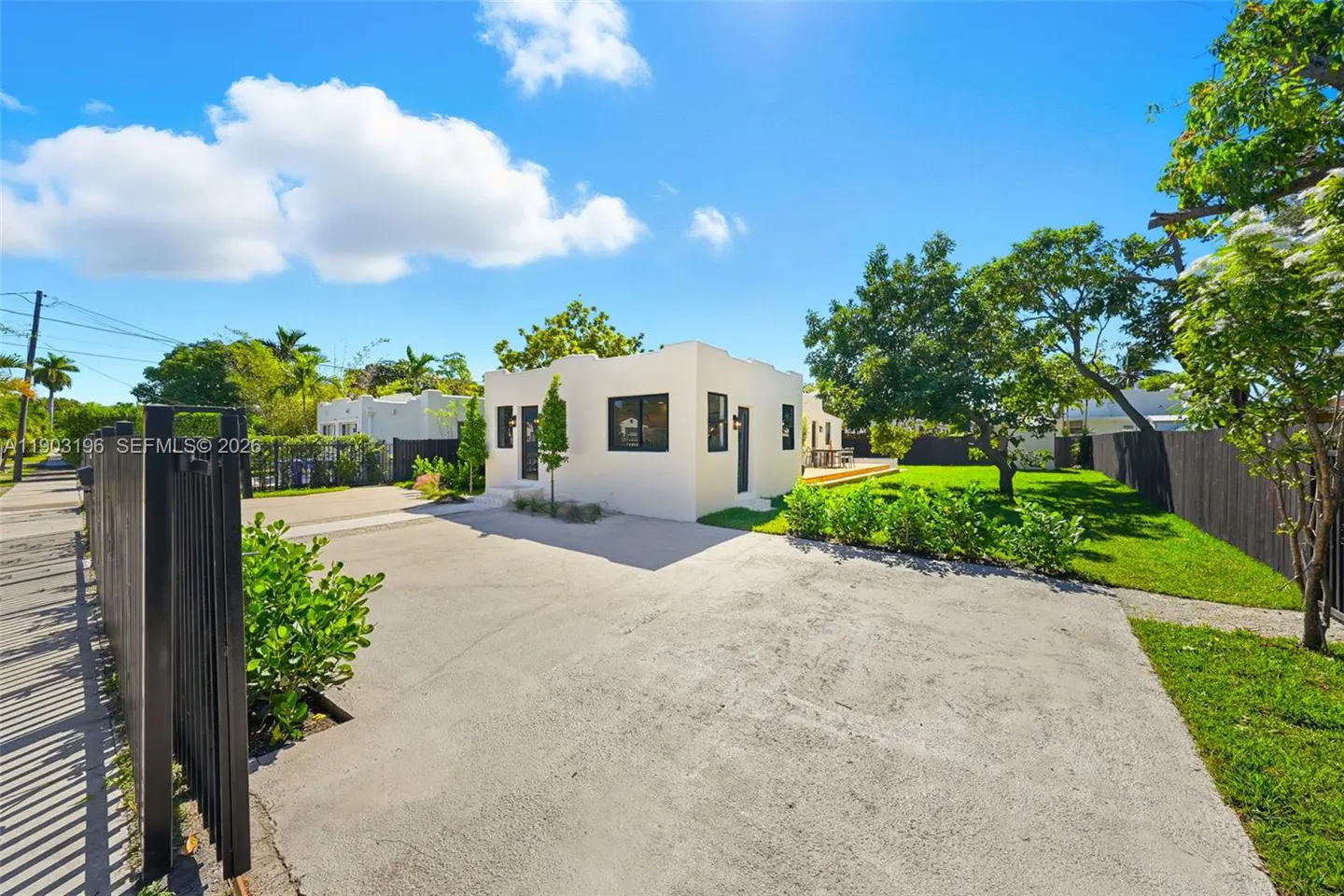Exterior view of a white, modern home with black trim, a concrete driveway, and green landscaping under a blue sky.
