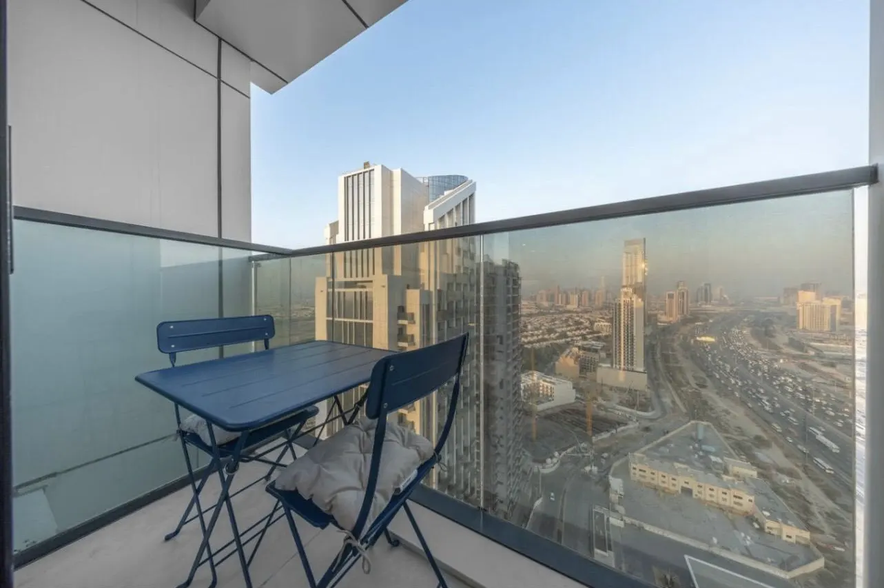 Balcony view with blue table and chairs overlooking a cityscape with tall buildings and a highway.