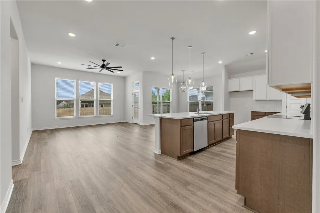 Open-concept kitchen and living area with light wood floors, white walls, a kitchen island, and modern pendant lighting.