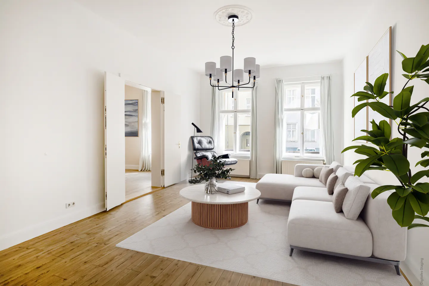 Bright living room with white walls, wood floors, and a white sectional sofa. A round coffee table sits on a marble rug, and a modern chandelier hangs from the ceiling.