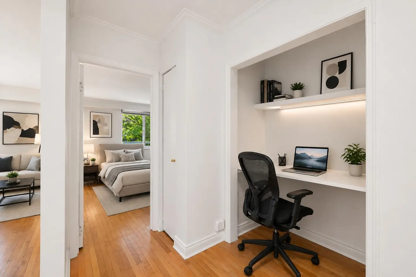 Bright, white home office nook with a black chair, laptop, and shelves. A bedroom and living room are visible in the background.