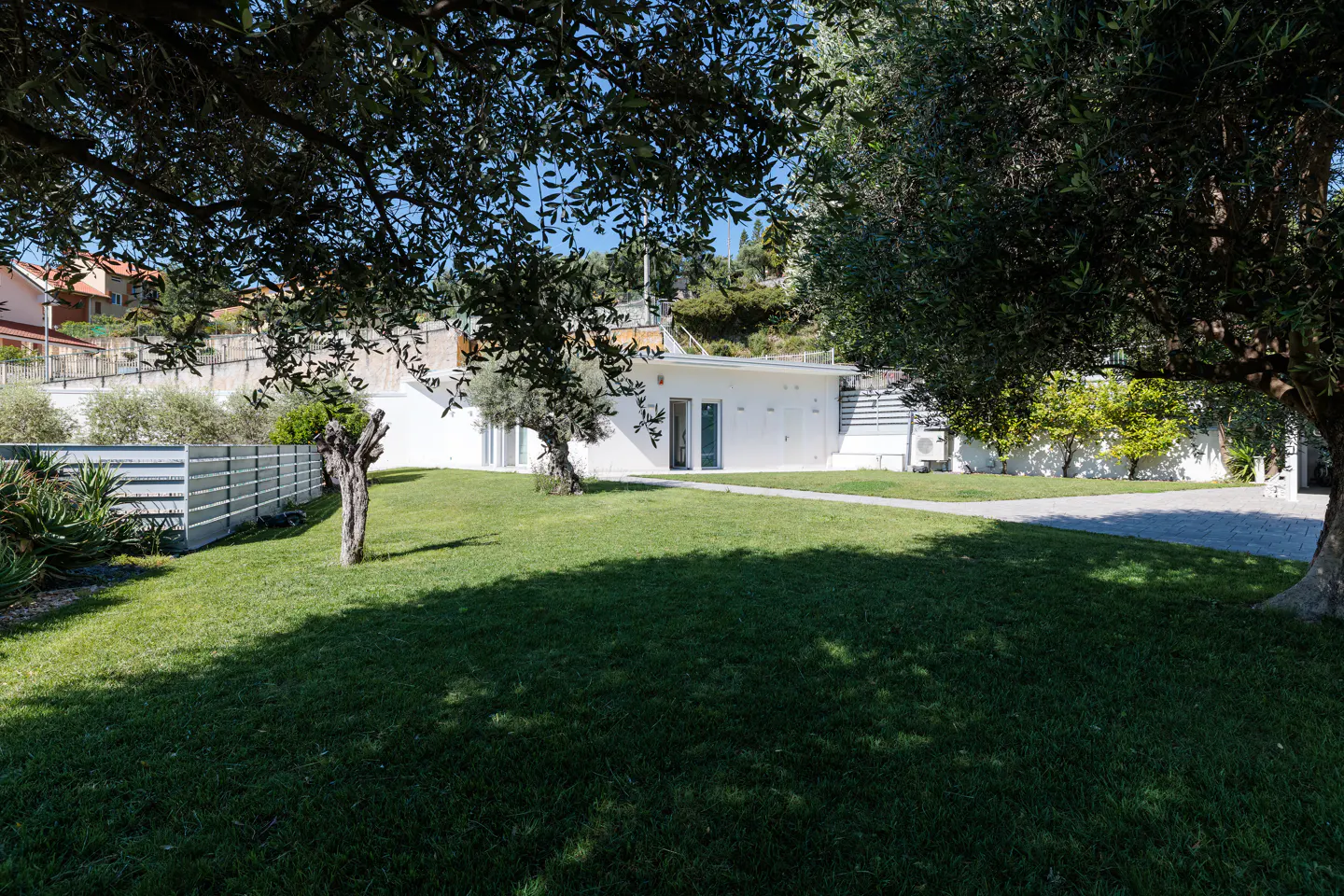 A modern white house with a green lawn, framed by trees. A stone path leads to the entrance.