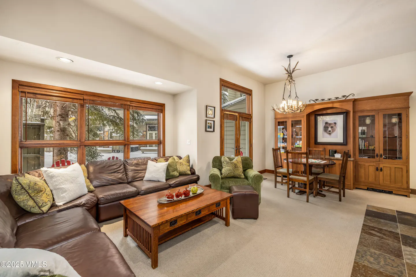 Living room with brown leather sectional, wood coffee table, green armchair, and dining set with a bear picture on the wall.