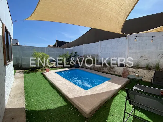 Backyard with a small blue pool, artificial grass, and a beige sunshade. A white fence and string lights are in the background.