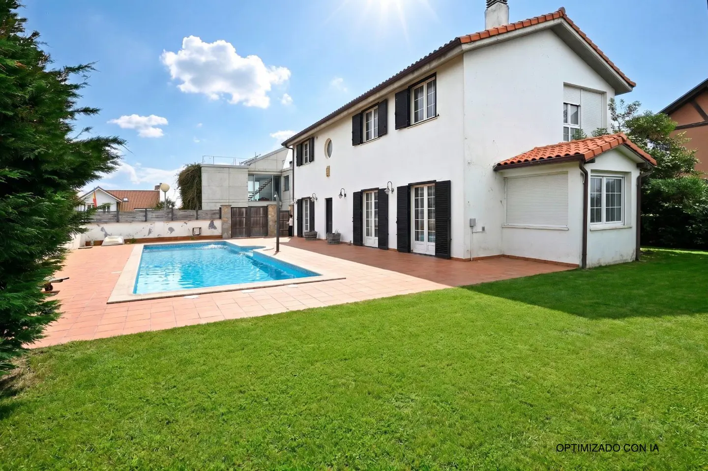 A white two-story house with black shutters, a red tile roof, and a blue swimming pool in the backyard.