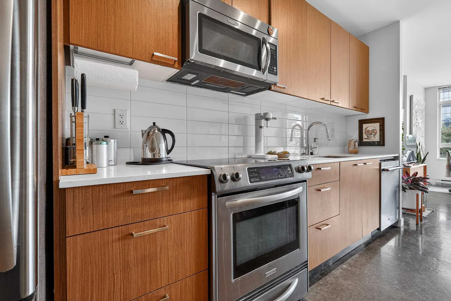 A modern kitchen with wood cabinets, stainless steel appliances, and white countertops.