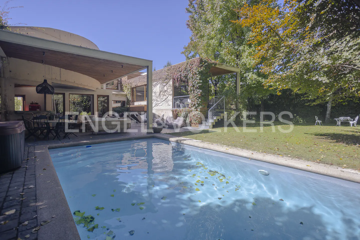 Outdoor pool with clear blue water, surrounded by patio, lawn, and modern house with green vines.