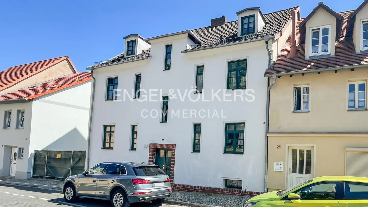 Exterior of a white, multi-story building with green window frames and a gray car parked in front. "Engel & Völkers Commercial" overlayed.