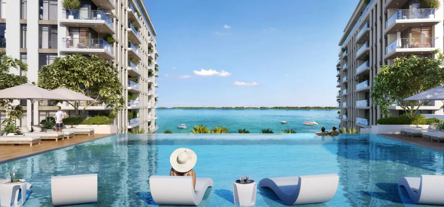 Infinity pool view between two condo buildings. Turquoise water extends to the horizon under a blue sky. White lounge chairs line the pool edge.