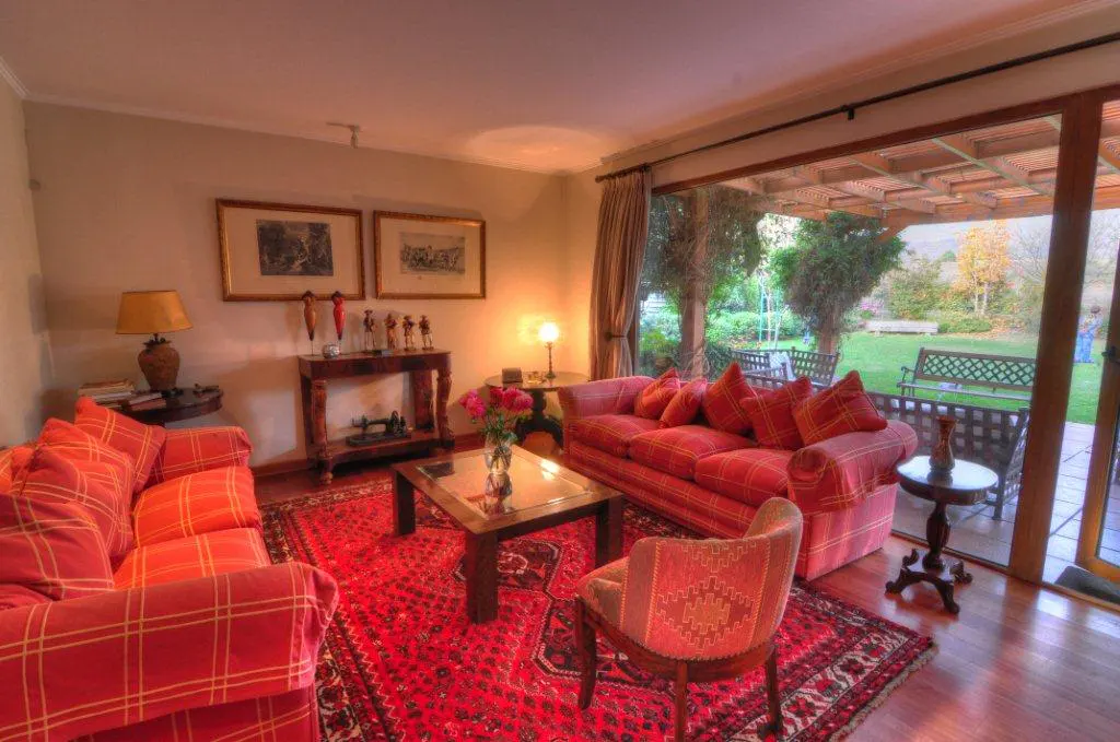 Cozy living room with red plaid sofas, a patterned rug, and a glass coffee table. A garden is visible through a large sliding glass door.