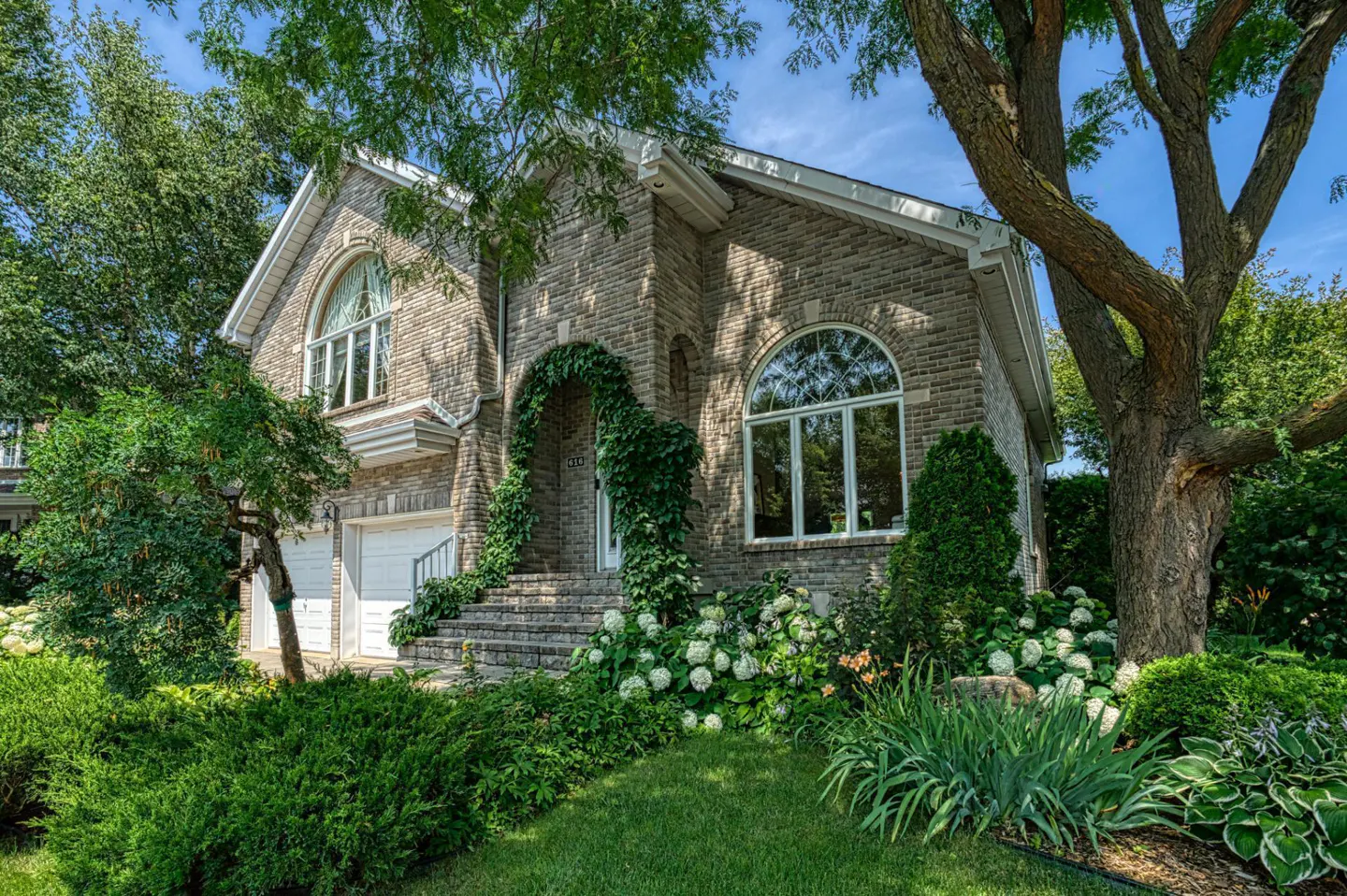 A two-story stone house with an arched doorway covered in ivy and a well-manicured lawn.