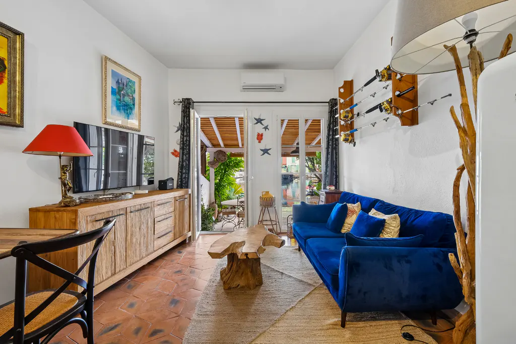 Living room with blue velvet sofa, wood table, and open doors to a patio. Fishing rods hang on the wall.