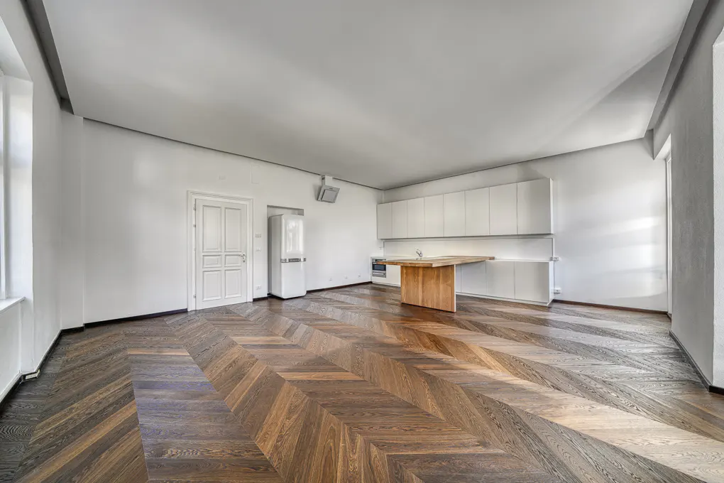 Minimalist kitchen with white cabinets, a wooden island, and dark chevron-patterned hardwood floors in a bright room.