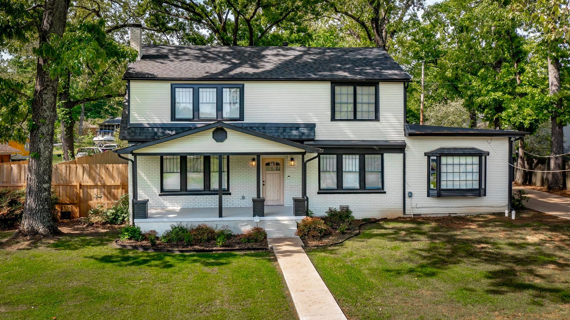 Two-story white house with black trim, a front porch, and a concrete walkway, surrounded by trees and a grassy lawn. [AI-generated text]