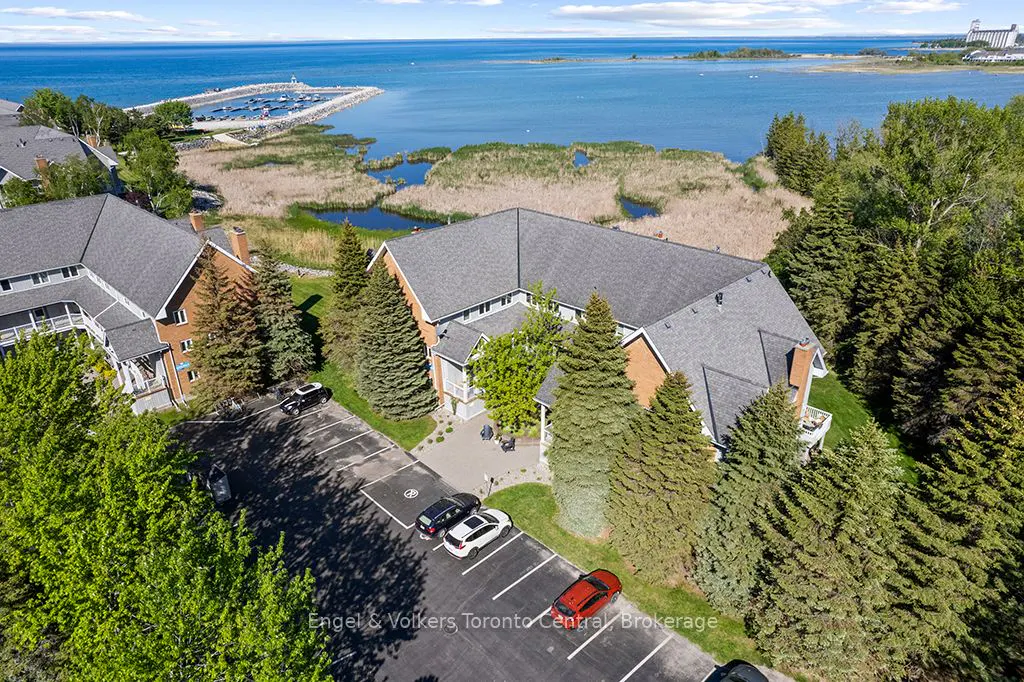 Aerial view of a multi-story residential building with a parking lot, surrounded by trees, marshland, and the blue lake.