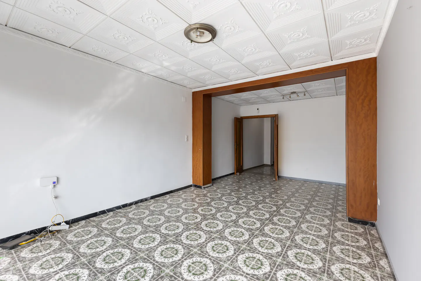 Empty room with white walls, patterned tile floor, and a brown wood doorway. A white, textured ceiling is overhead.