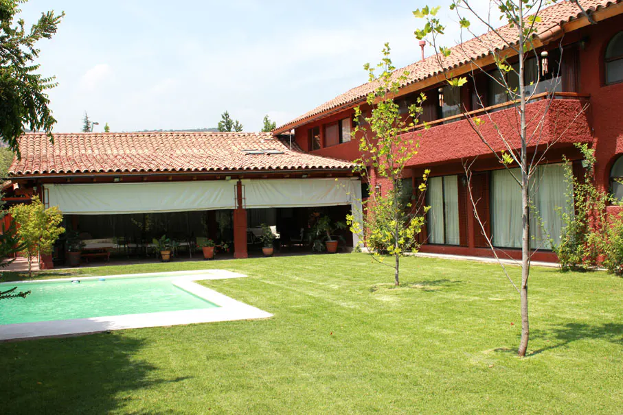 Exterior view of a red two-story house with a pool, green lawn, and a covered patio with white shades.