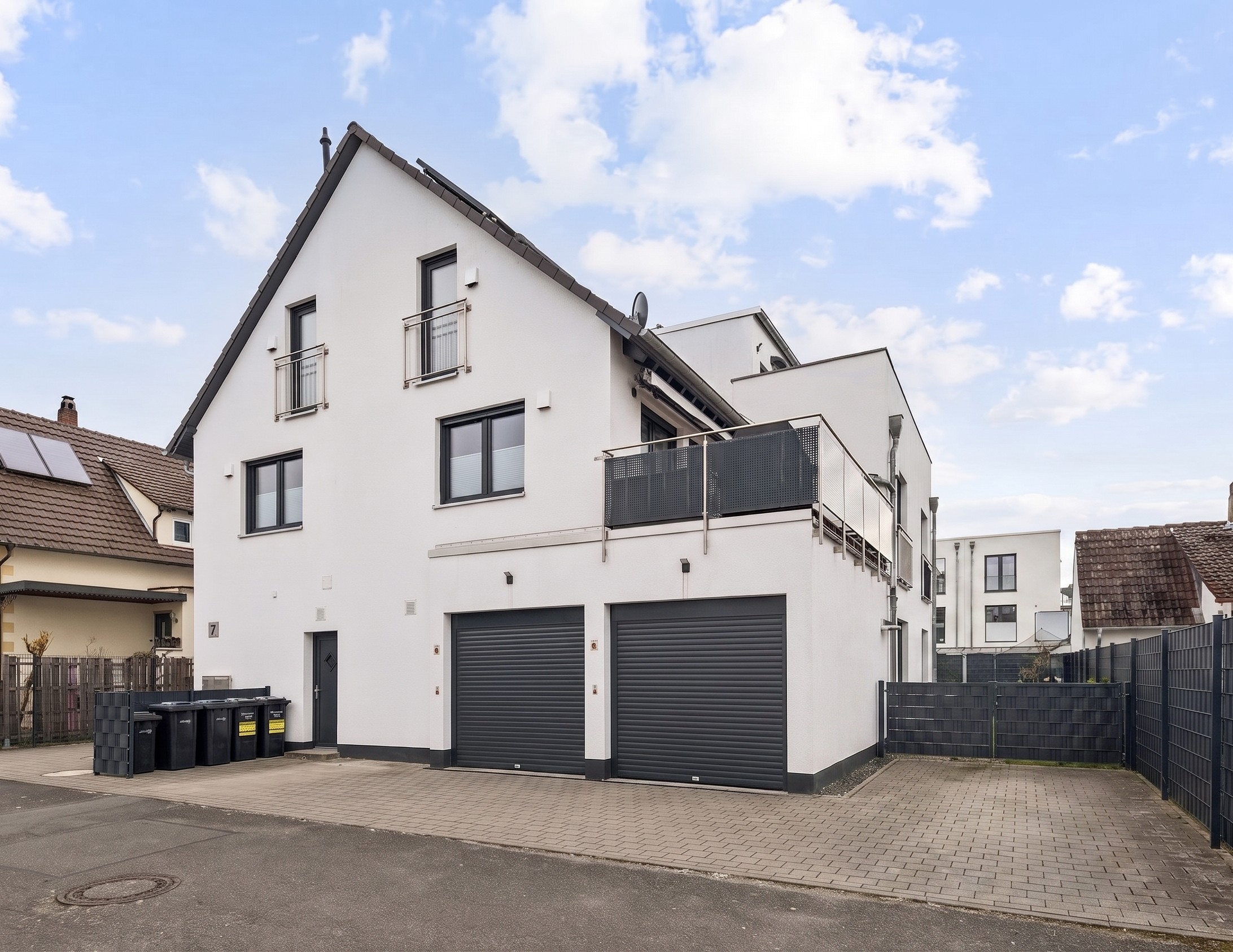 Exterior view of a modern, white two-story house with a gray roof, two garage doors, and small balconies.