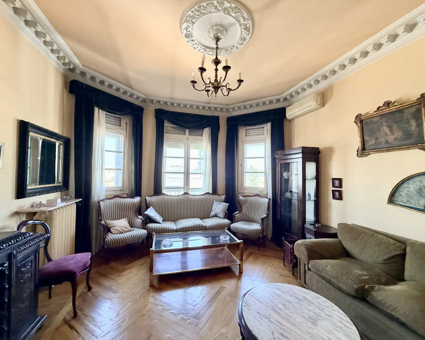 Living room with parquet floor, striped sofas, dark blue curtains, and a chandelier.