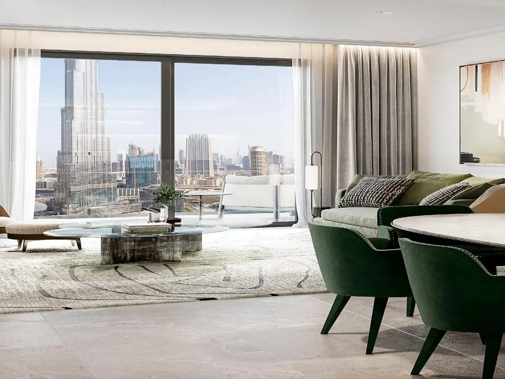 Living room with a view of Dubai. The Burj Khalifa is visible through a large window. Green chairs and sofa.
