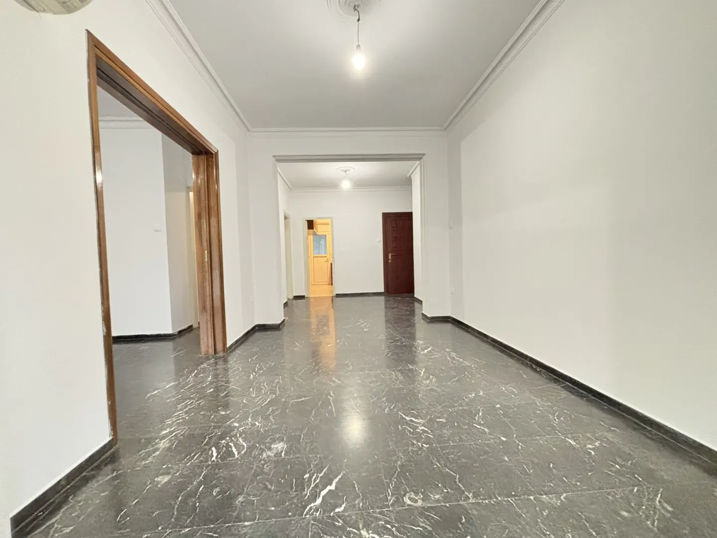 Empty room with white walls, black marble floor, and wooden door frames. A light fixture hangs from the ceiling.