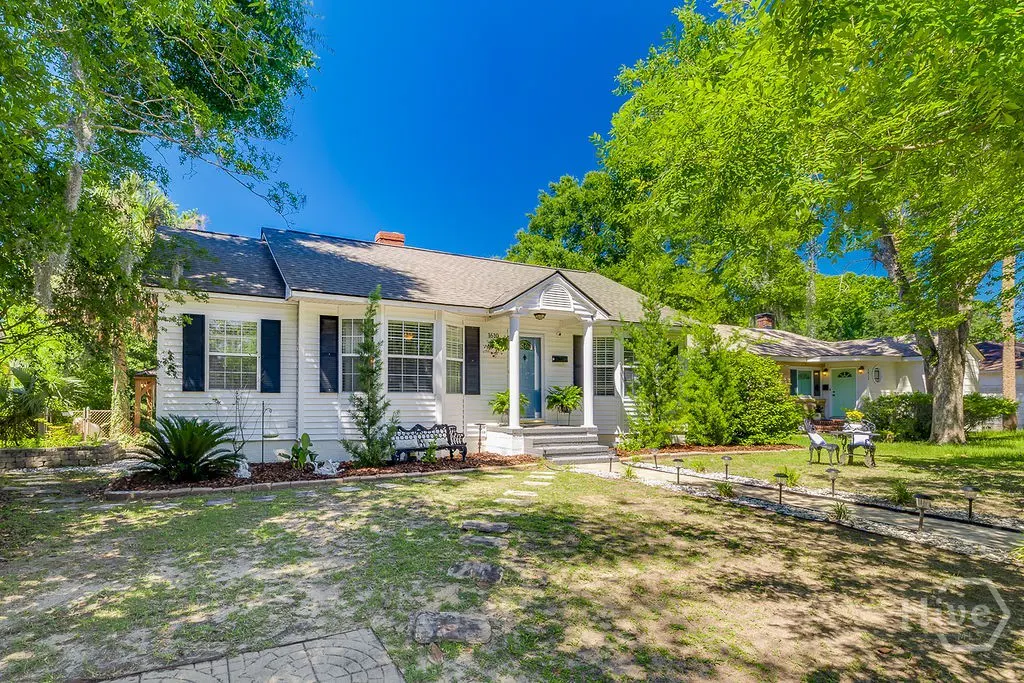 White single-story home with blue shutters, a front porch, and a grassy yard under a clear blue sky.