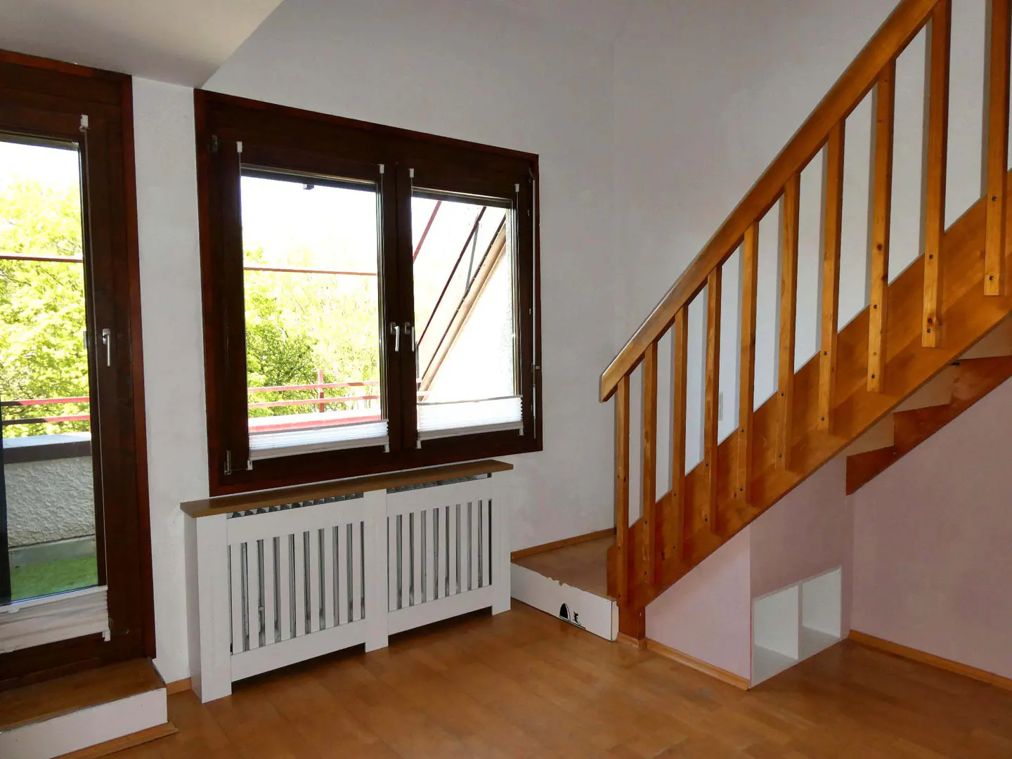 Interior view with wood floors, brown window frames, and a wooden staircase with white storage underneath.