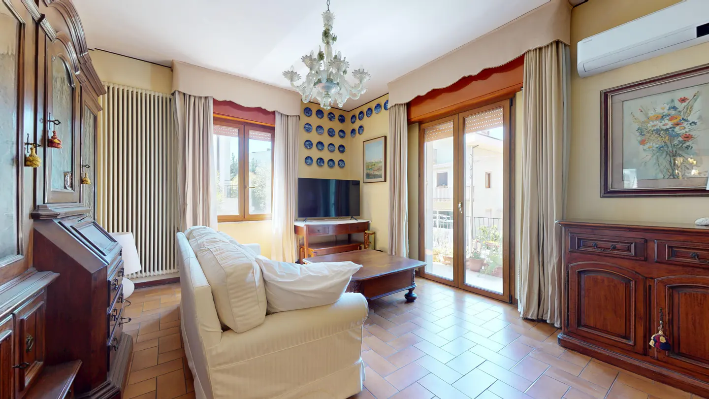A living room with a white sofa, TV, chandelier, and wooden furniture.