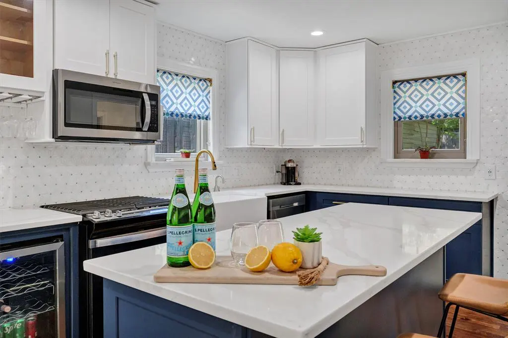 Bright kitchen with white cabinets, blue island, and marble countertops. Pellegrino bottles and lemons sit on a wooden board.