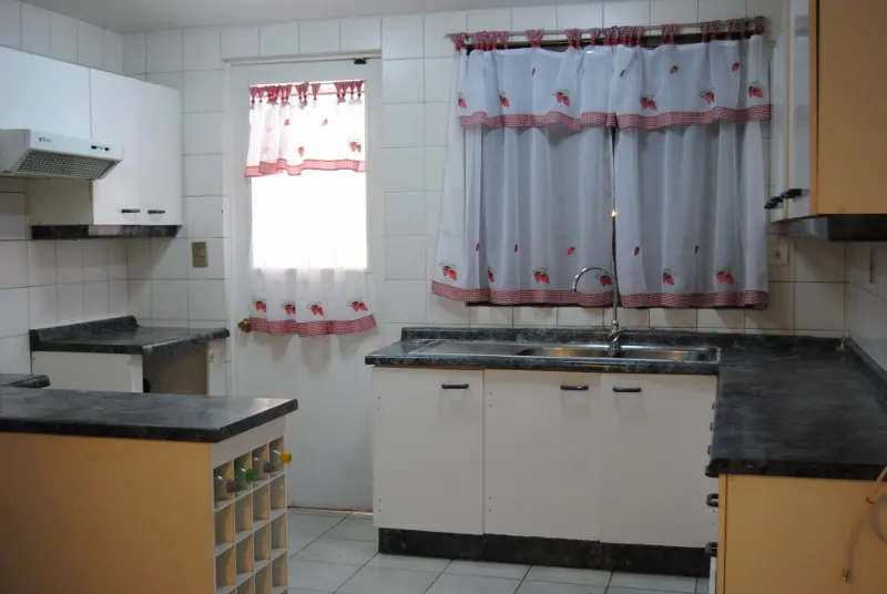 A kitchen with white cabinets, dark countertops, and strawberry-patterned curtains on the window.